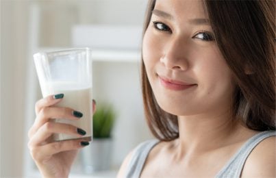 a woman holding a glass of milk while looking at the camera