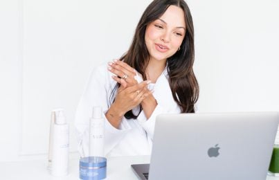 a woman using her laptop while applying cream on her hand