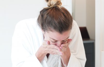 Woman splashing her face with water at a sink