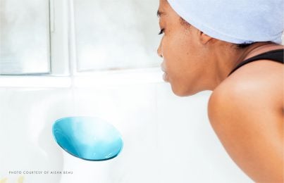 Woman leaning over handheld face steamer device