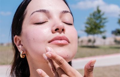 a girl standing outside in the sun touching her summer skin breakout
