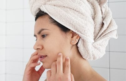 a woman standing in the shower touching her face with concern